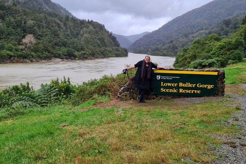 Una persona de pie junto a un cartel del Parque Escénico Lower Buller Gorge. 2