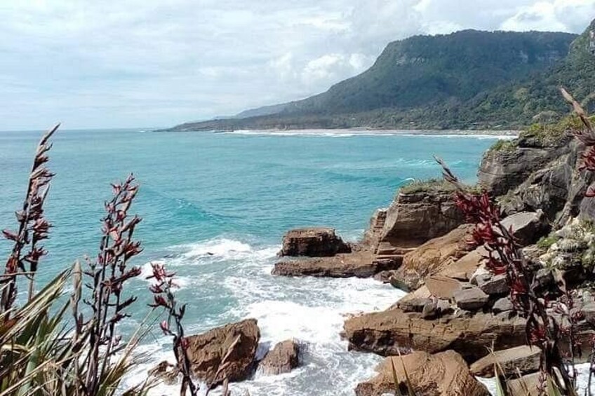 Un paisaje costero con formaciones rocosas, olas rompiendo en la orilla y una cadena montañosa distante. 3
