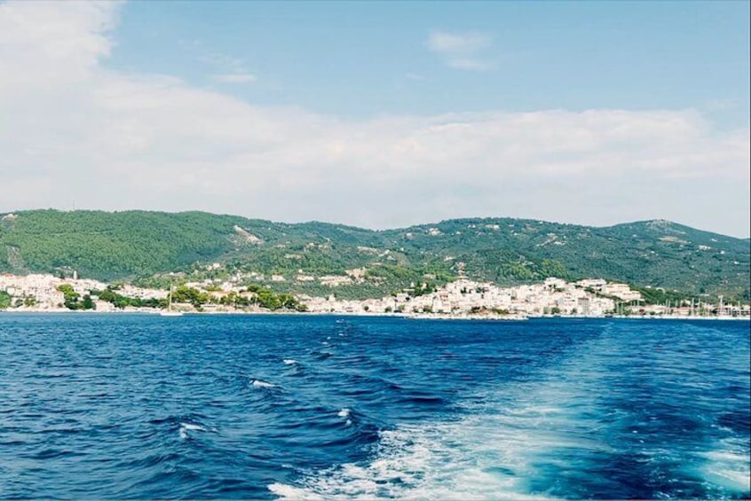 A coastal town with buildings, a body of water, and green hills in the background. 3