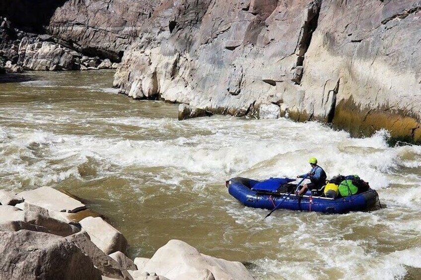 A person in a blue raft navigating a river with white water rapids, surrounded by rocky cliffs. 4