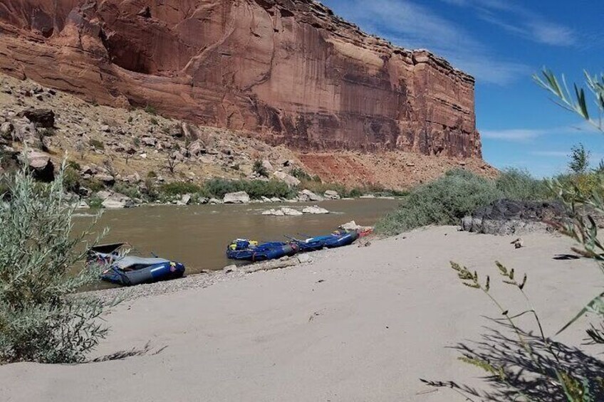 A river with kayaks and a red rock cliff. 3