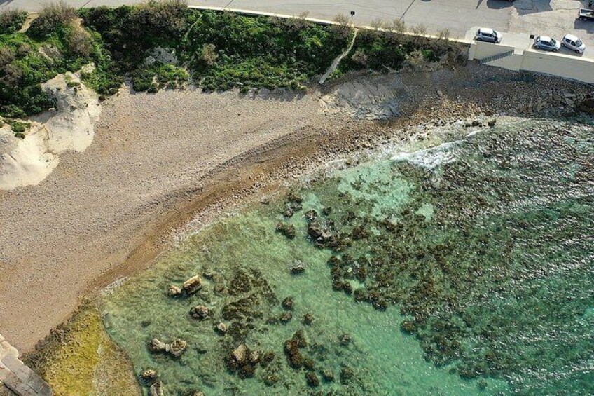 A beach with clear water, rocky areas, and a parking lot with cars. 3