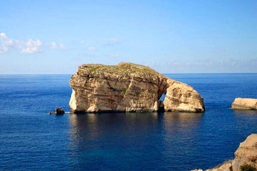 A large rock formation in the sea with clear blue water around it. 4