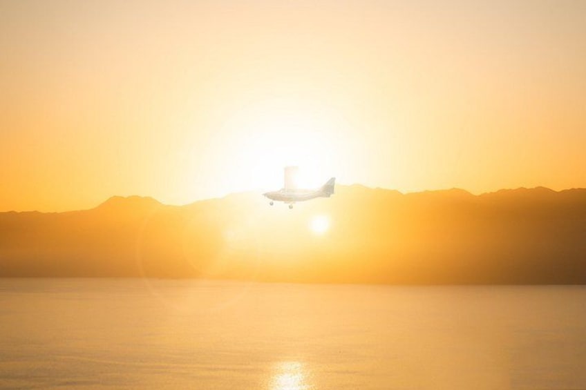 A helicopter flying over a body of water with a mountain range in the background during sunset. 1
