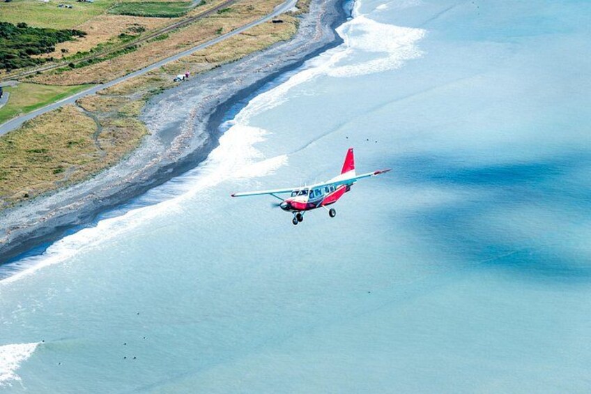 A small aircraft flying over a coastal area with a beach and a road. 3