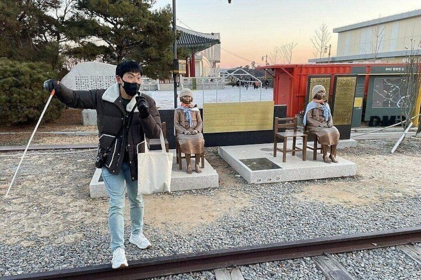 A person taking a photo with a camera, a statue of a woman, and a train track. 1