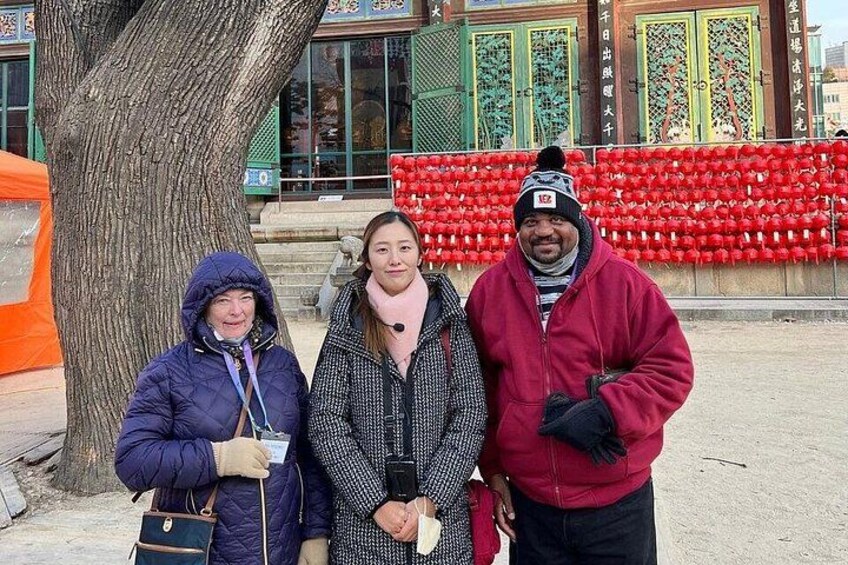 Trois personnes se tiennent devant un arbre et un bâtiment décoré de rouge. 2