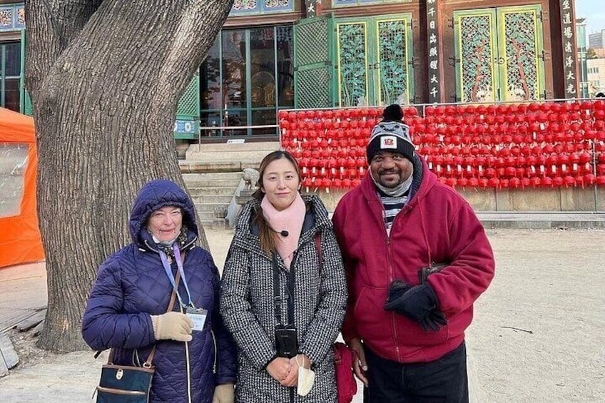Three people standing in front of a tree and a building with red decorations. 2