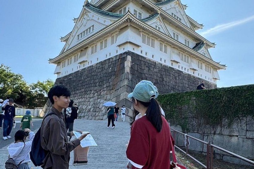A historic castle with tourists, a stone wall, and a paved walkway. 1