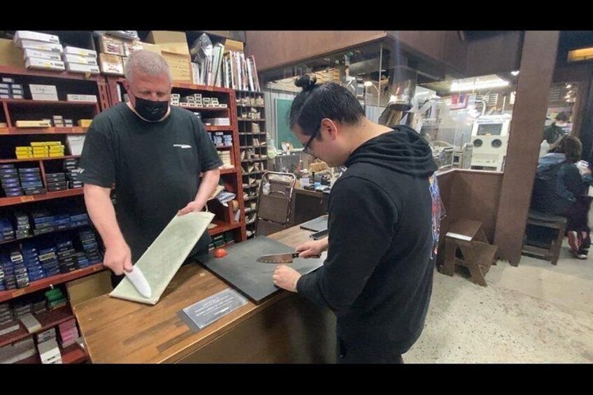 Two people at a counter in a workshop with shelves of tools and materials. 2