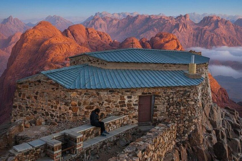 A stone building with a blue roof on a mountain peak, overlooking a vast mountain range. 2