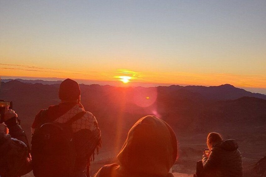 A sunset over a mountainous landscape with people observing the sun. 4