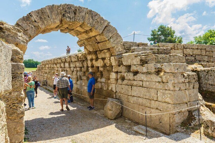 Ancient stone ruins with an arched entrance, visitors walking around, and a clear sky. 3