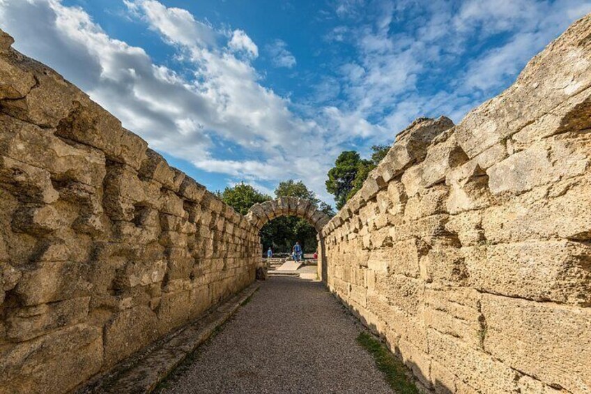 A stone pathway flanked by ancient walls, leading to an arched gateway. 2