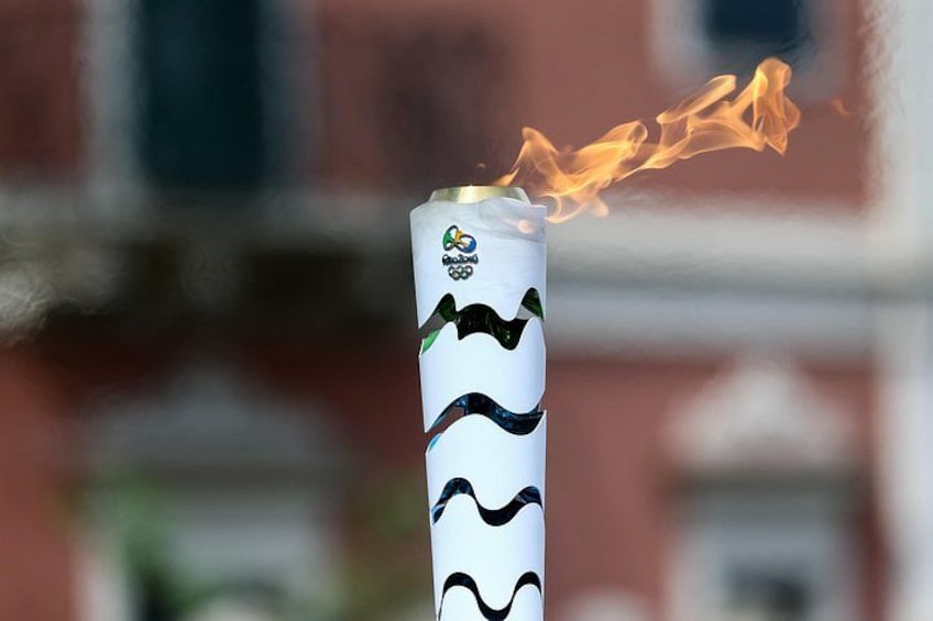 A can with a flame at the top, set against a blurred background with buildings. 2