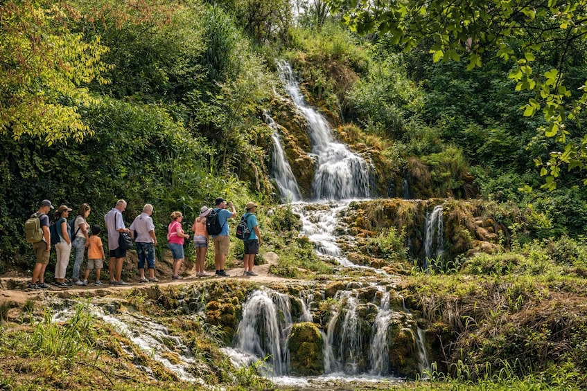 A group of people standing on a path observing a multi-tiered waterfall surrounded by lush greenery. 3