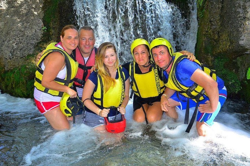 A group of people wearing life jackets and helmets near a waterfall. 5