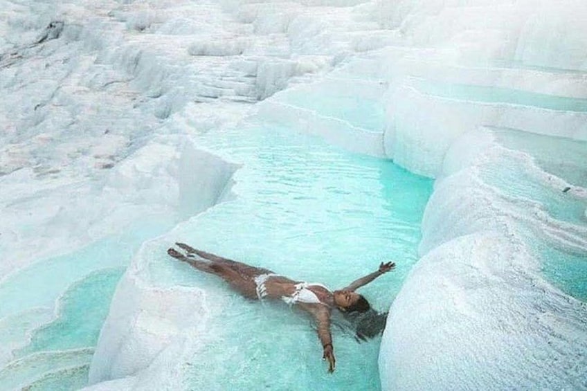 Una persona flota en una piscina turquesa rodeada de terrazas de travertino blanco. 3