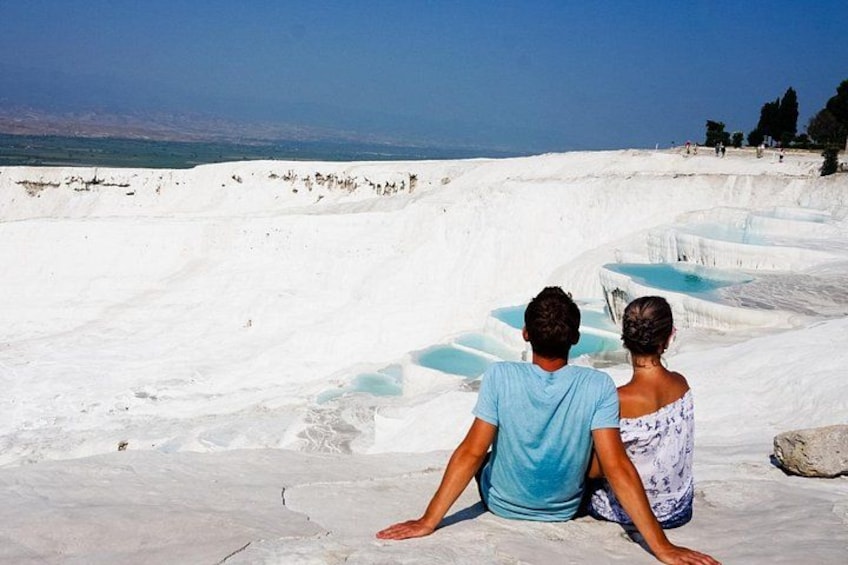 Dos personas sentadas sobre un paisaje blanco escalonado con estanques de agua. 4