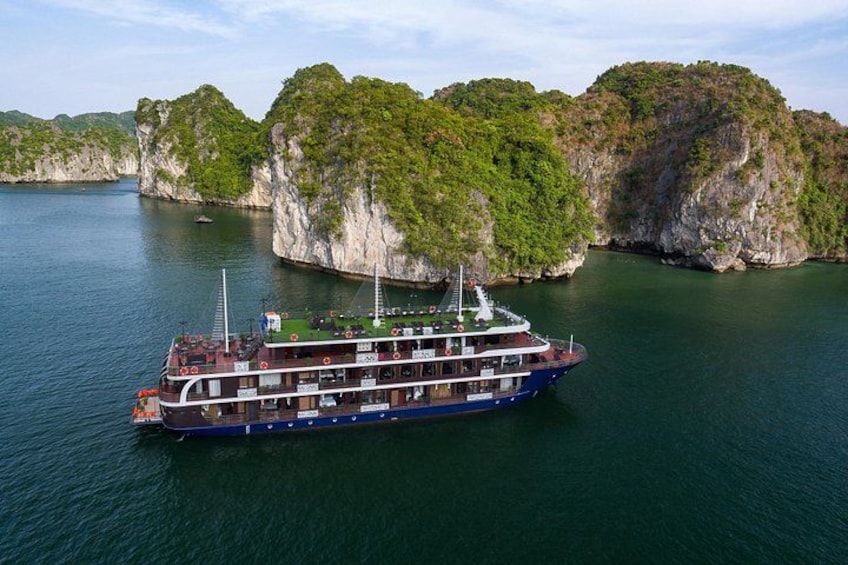 A large boat with multiple decks on a calm body of water surrounded by rocky cliffs. 2