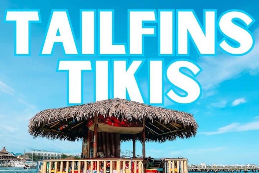 Estructura de techo de paja con el texto 'TAILFINS TIKIS' contra un cielo azul despejado. 2