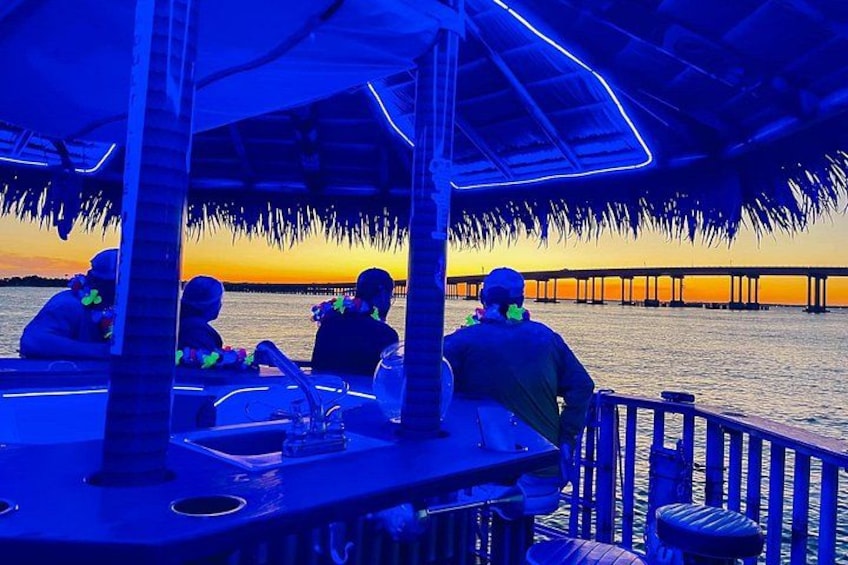 A boat with a thatched roof, people on board, and a sunset in the background. 2