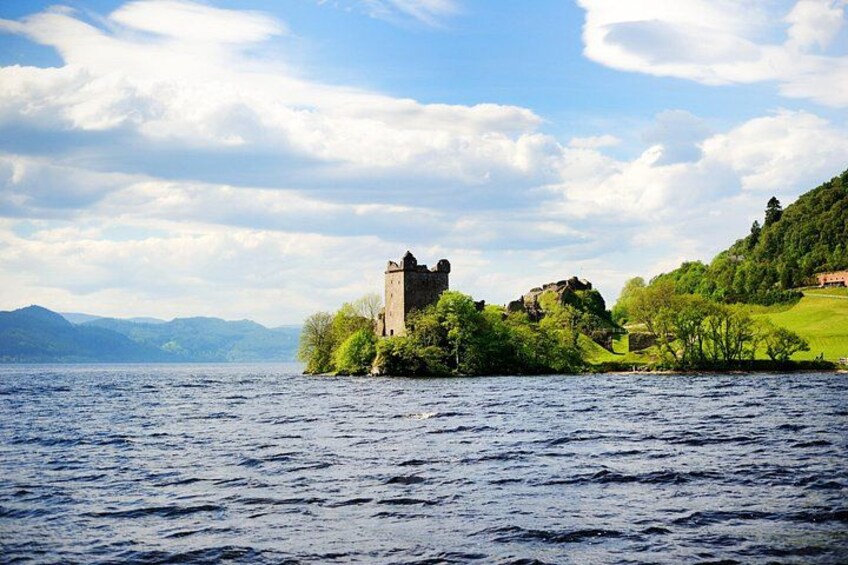 Un château se dresse sur une île verdoyante, entourée d’eau, avec des montagnes en arrière-plan. 5