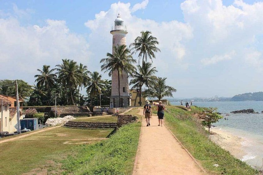 Een vuurtoren, palmbomen, een strand en een pad. 3