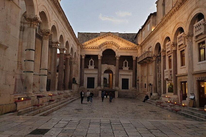 A courtyard with classical architecture, including columns and arches, and a few people walking. 3