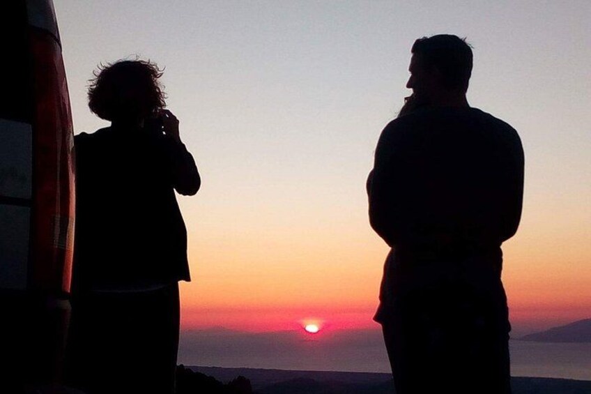 Silhouetten van twee personen staan bij zonsondergang, met een zichtbare zon en een berg op de achtergrond. 2