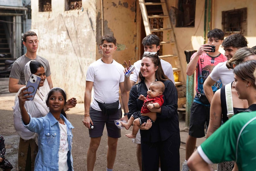 A group of people standing outdoors, some holding a baby, with a building in the background. 1