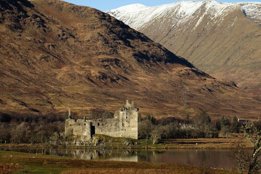 A historic stone castle by a lake with a snow-capped mountain in the background. 4