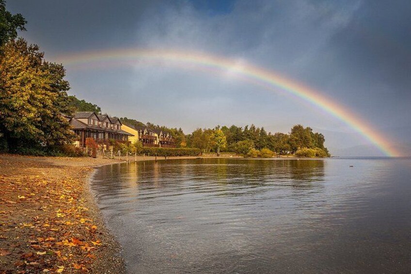Un lago con un arcobaleno, foglie autunnali e case lungo la riva. 4