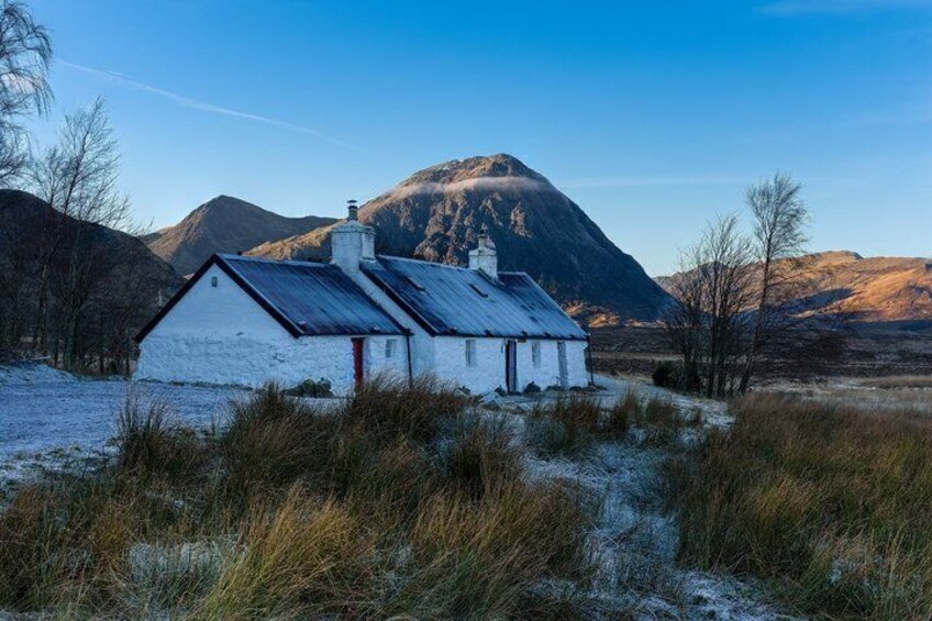 Una casa bianca con una porta rossa, circondata da erba e montagne sullo sfondo. 1