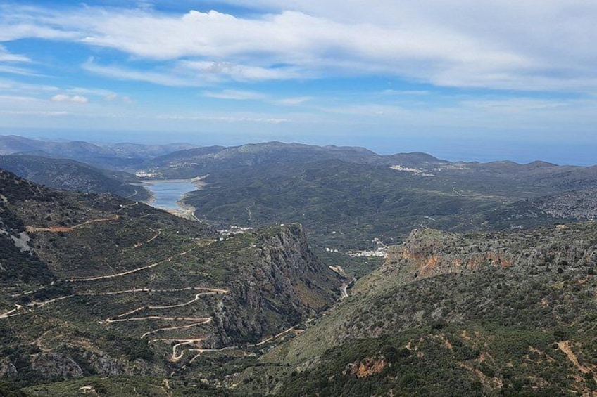A mountainous landscape with winding roads, a river, and distant buildings. 5