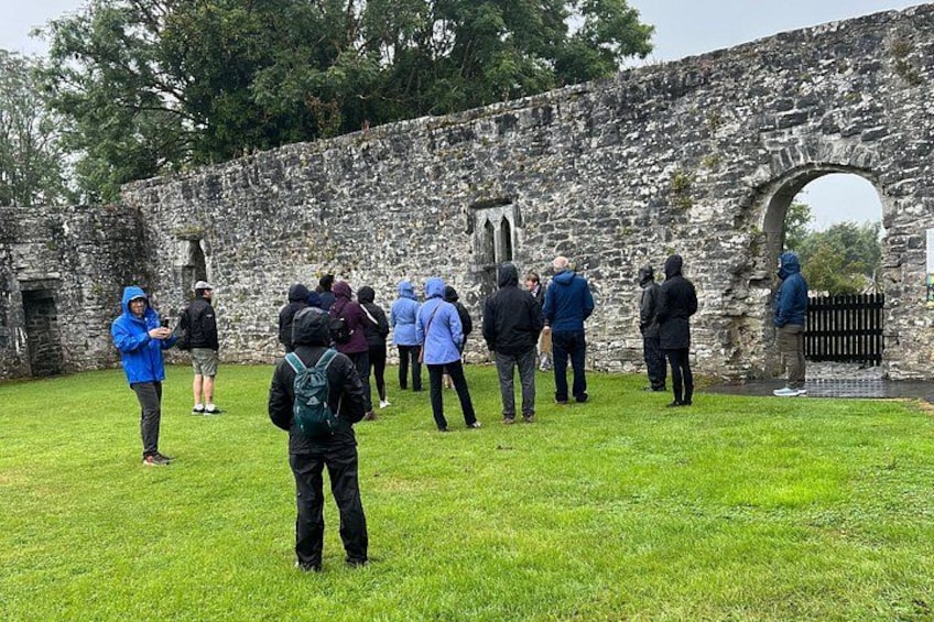 A group of people standing in front of a stone wall with an archway, possibly at a historical site. 3