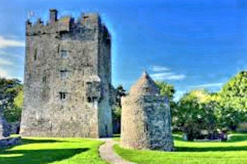A large stone castle with a smaller tower, surrounded by a well-maintained lawn and trees. 2