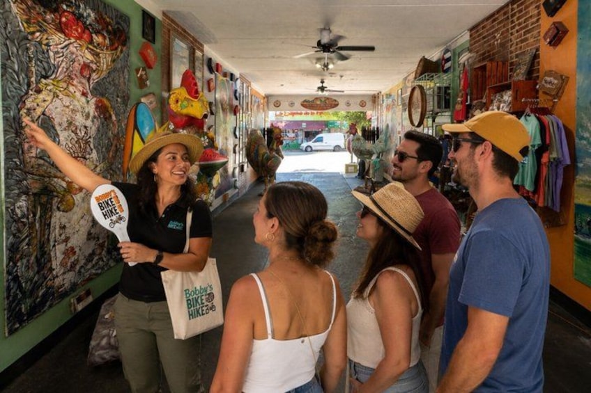 Un gruppo di persone cammina lungo un corridoio decorato con murales colorati e costellato di negozi. 5