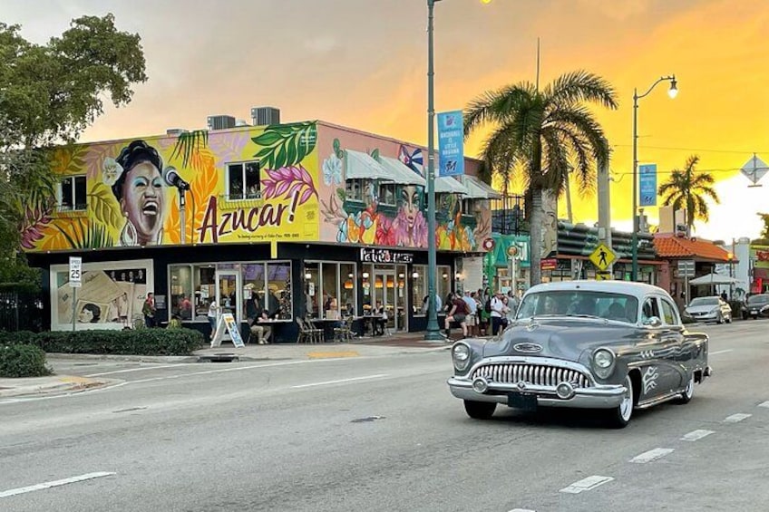 Un'auto d'epoca che percorre una strada con un murale colorato su un edificio. 1