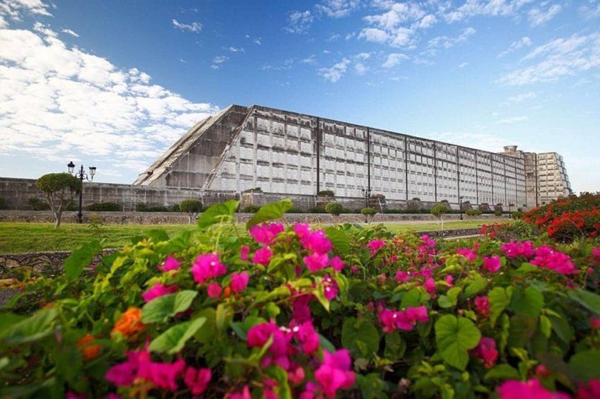 A large building with a sloped roof, surrounded by a well-maintained garden with vibrant pink flowers. 3