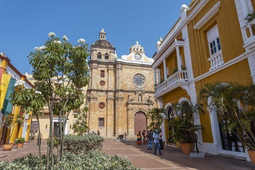 Una iglesia histórica con una torre de reloj, rodeada de palmeras y edificios con fachadas amarillas y blancas. 2