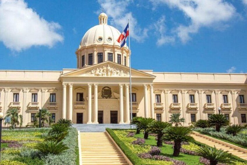 A large, classical building with a dome and columns, surrounded by a well-maintained garden with palm trees and flowers. 5