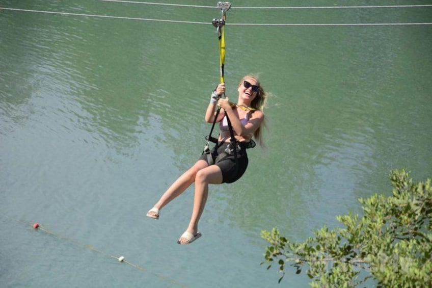 Een persoon beoefent watersport, opgehangen aan een tuig en touw, met een wateroppervlak en begroeiing op de achtergrond. 4