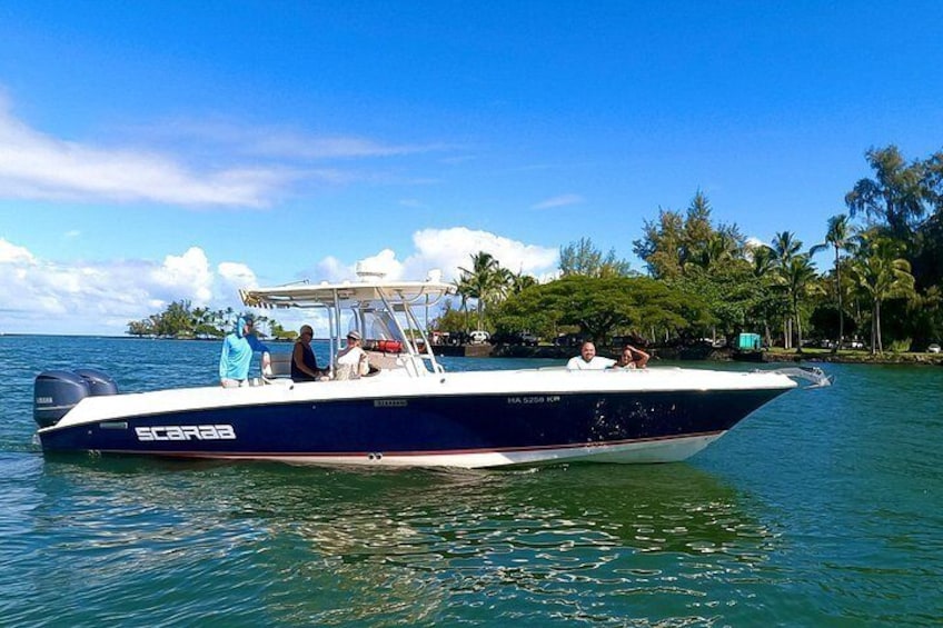 Un bateau à moteur rapide, baptisé « SCARAB », navigue sur une eau calme, sous un ciel dégagé, avec un paysage tropical en arrière-plan. 5