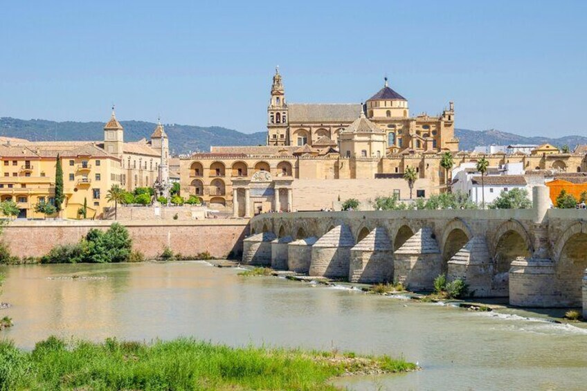 A historic building with arches, a river, and a bridge. 2