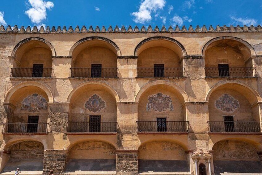 A building with multiple arched windows and balconies, featuring intricate stonework and a tiled roof. 4