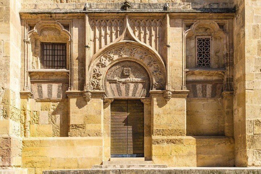 A stone building with an ornate archway, a small window, and a door. 3