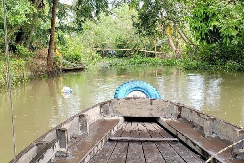 Una balsa de madera con un neumático azul en la parte trasera, flotando sobre un río tranquilo rodeado de abundante vegetación. 3