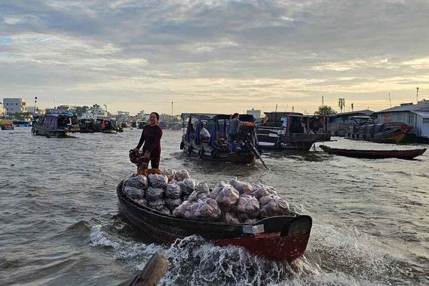 Un bote transporta sacos de mercancía por un río, con otras embarcaciones y construcciones al fondo. 5