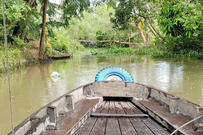 Ein hölzernes Boot mit blauem Reifen im Wasser, umgeben von Grünpflanzen und einer kleinen Brücke. 4